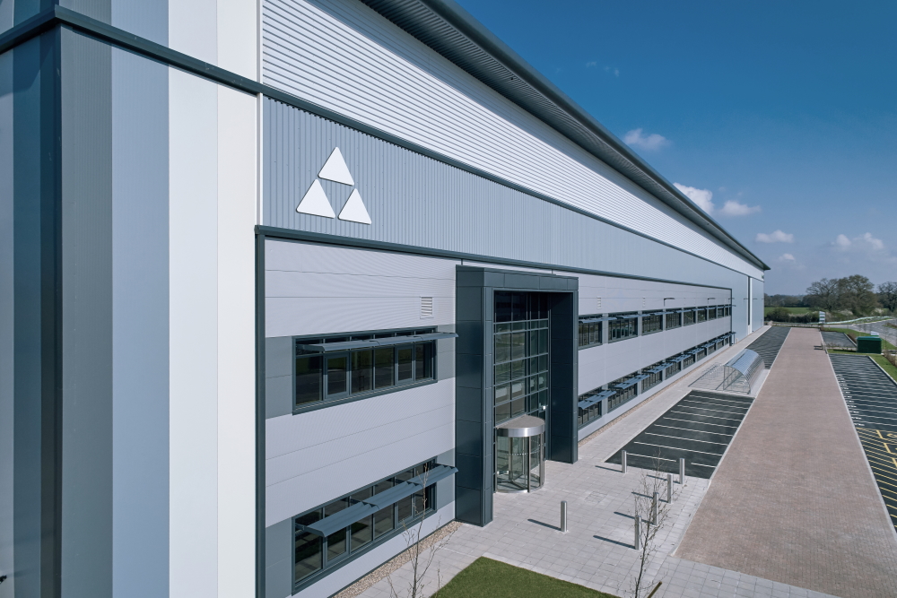 This image: a building at Symmetry Park, Bicester. The map: there is a green marker inside a red line boundary, indicating the site of the proposed Hinckley National Rail Freight Interchange, with Nuneaton to the west and Leicester to the north-east.